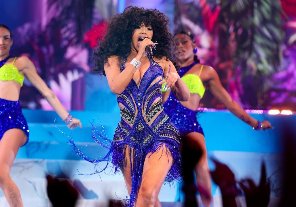 Rapper Cardi B performing onstage in colorful blue outfit among backup dancers.