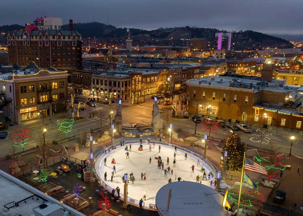 skaters on an outdoor ice rink in foreground of rapid city at dusk