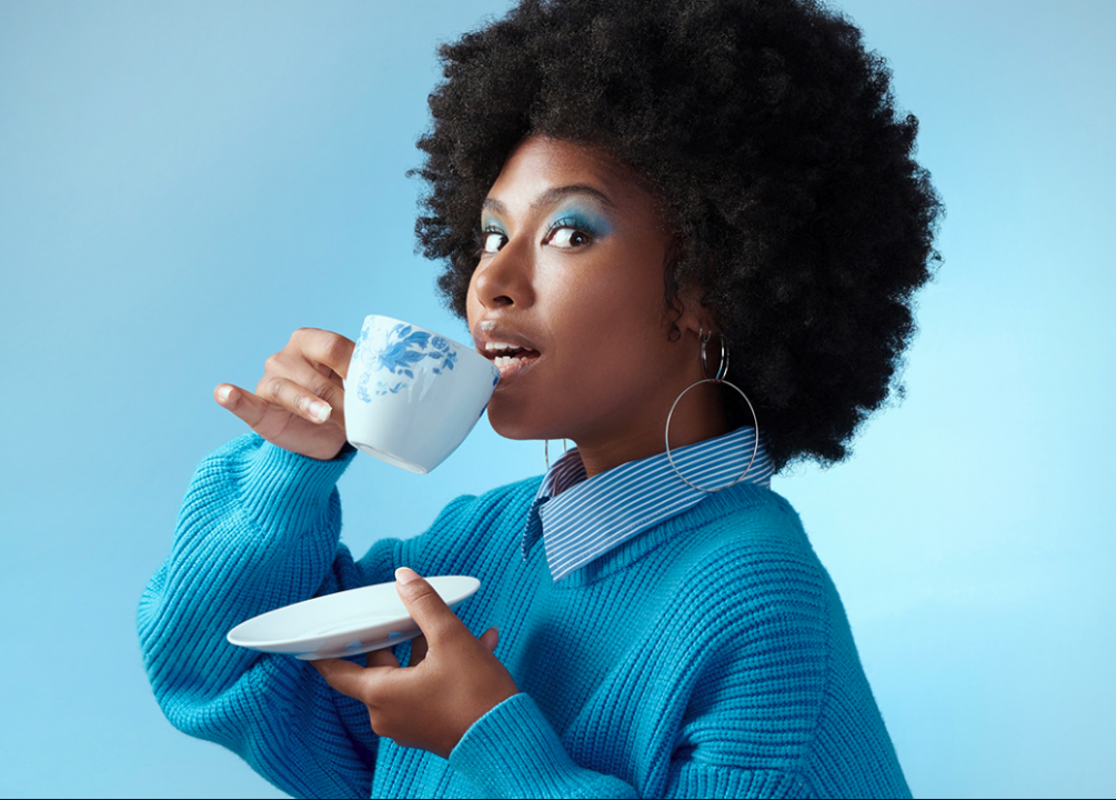 A Black woman with a teacup against a bright blue background.