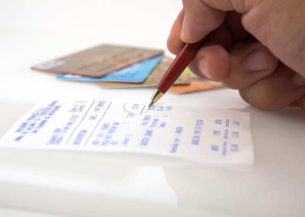 pen in hand circling receipt totals with credit cards in background
