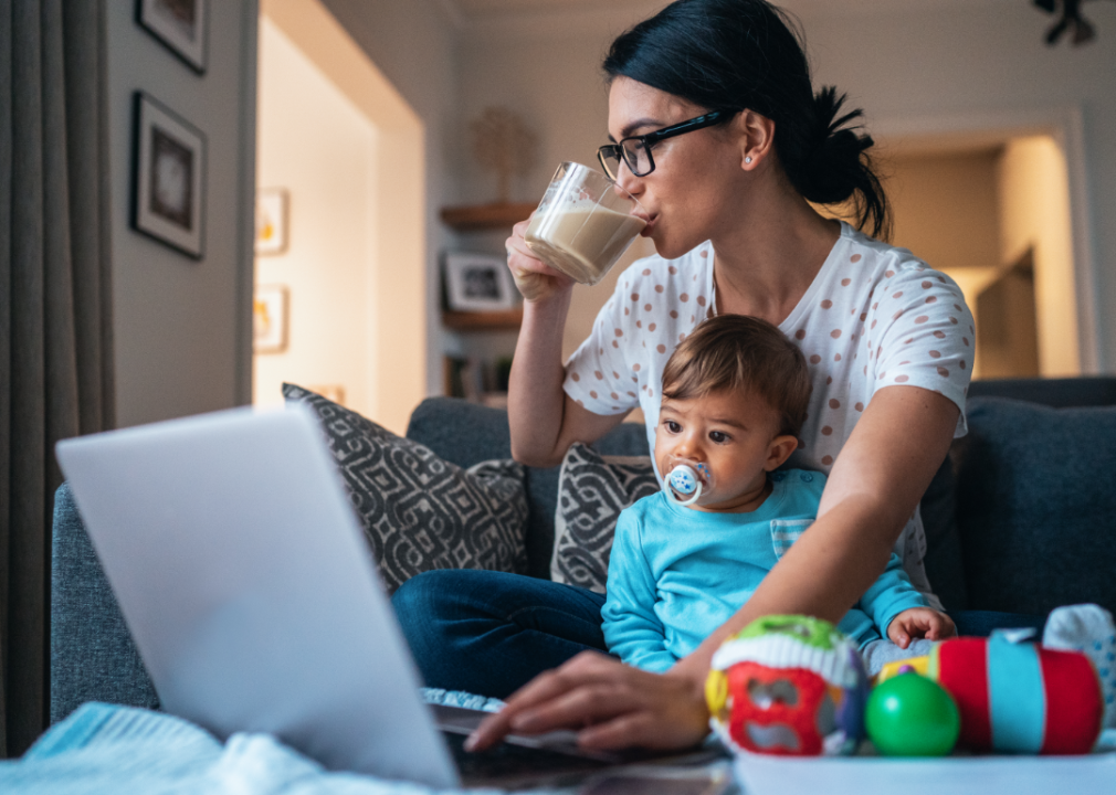 Mom with a baby drinking coffee while working at home with a laptop