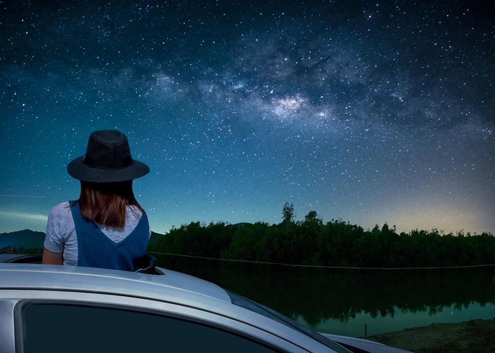 person viewing night sky full of stars by standing up in sunroof 