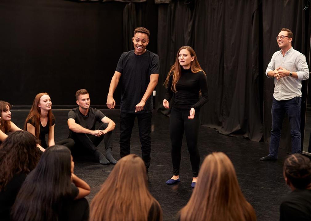 A teacher and a group of drama students rehearsing during a performing arts class.