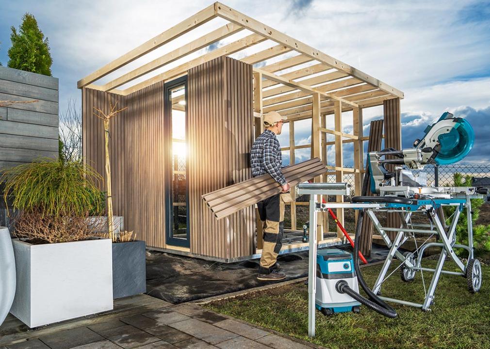 Woodworker with equipment building a modern backyard garden shed.