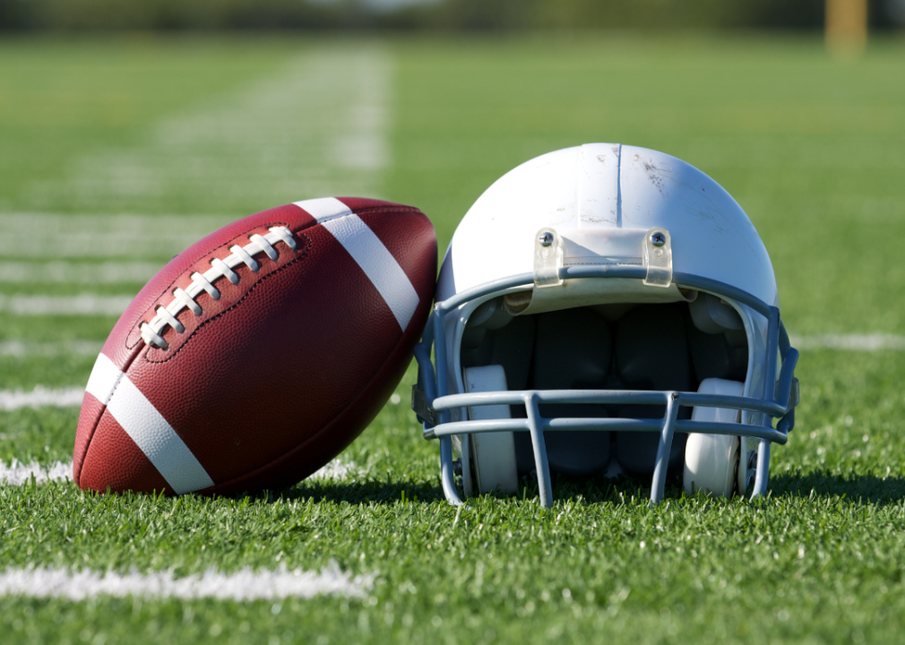 A football rests against a helmet on a football field.