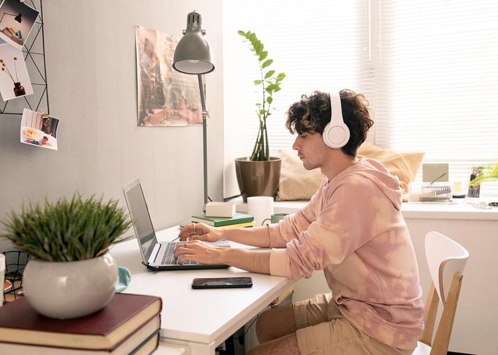 Person wearing headphones and pink tie-dye sweatshirt works peacefully on laptop in room with window light.