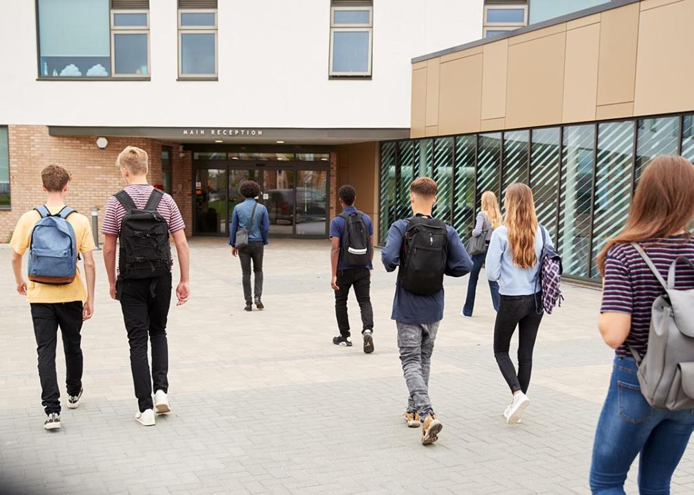 Eight students walking towards the main entrance of a school.