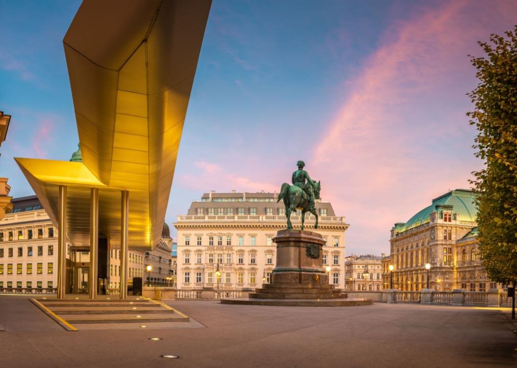 Square with a statue in front of muesum Albertina in Vienna with historical Hotel Sacher and Vienna state opera in the background.