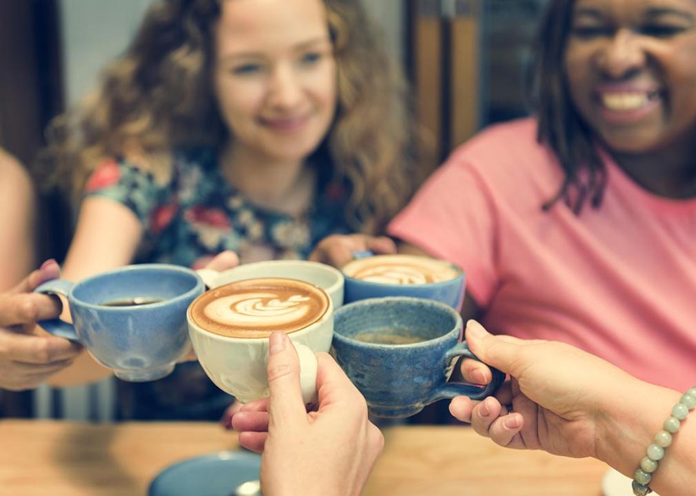 Five hands holding coffee touch their drinks together in the middle of the table with two women
