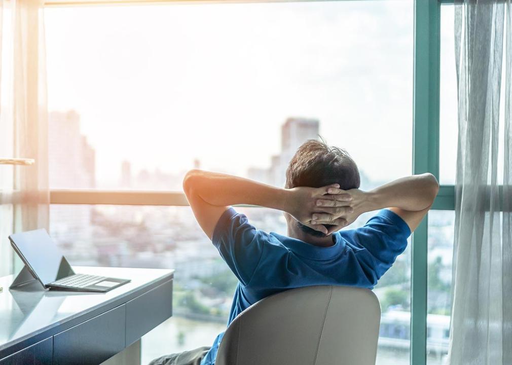 A student with laptop relaxing in a hotel room overlooking a skyscraper.