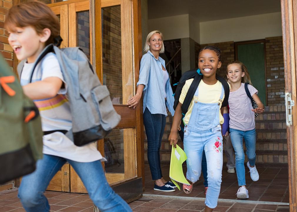 Why does student mental health suffer during summer? Here's what the data says Smiling elementary school-age students run out of a school from a door held open by a teacher.