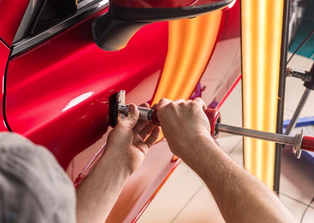 A worker performing dent repairs on the door of a red car.