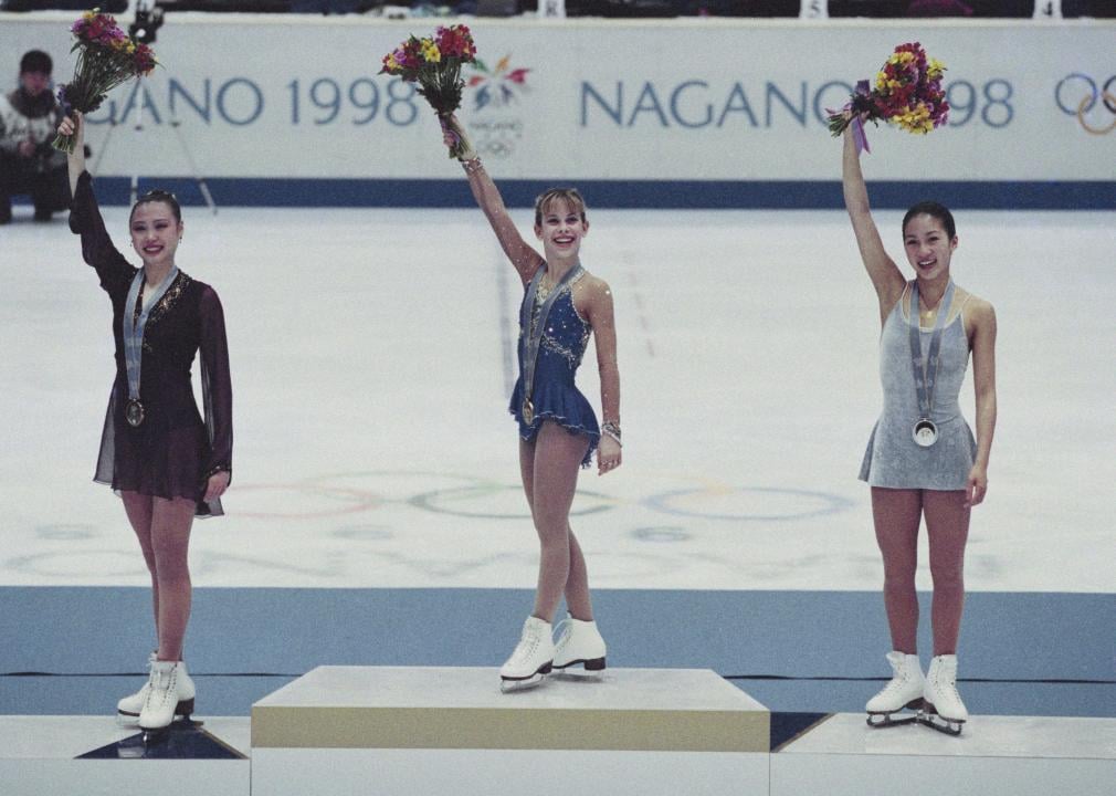 Bearing the gold medal on the Olympic podium, Tara Lipinski of the United States (center) raises her arm with a bouquet of flowers alongside silver medalist Michelle Kwan (right) and bronze medallist Chen Lu of Chin.