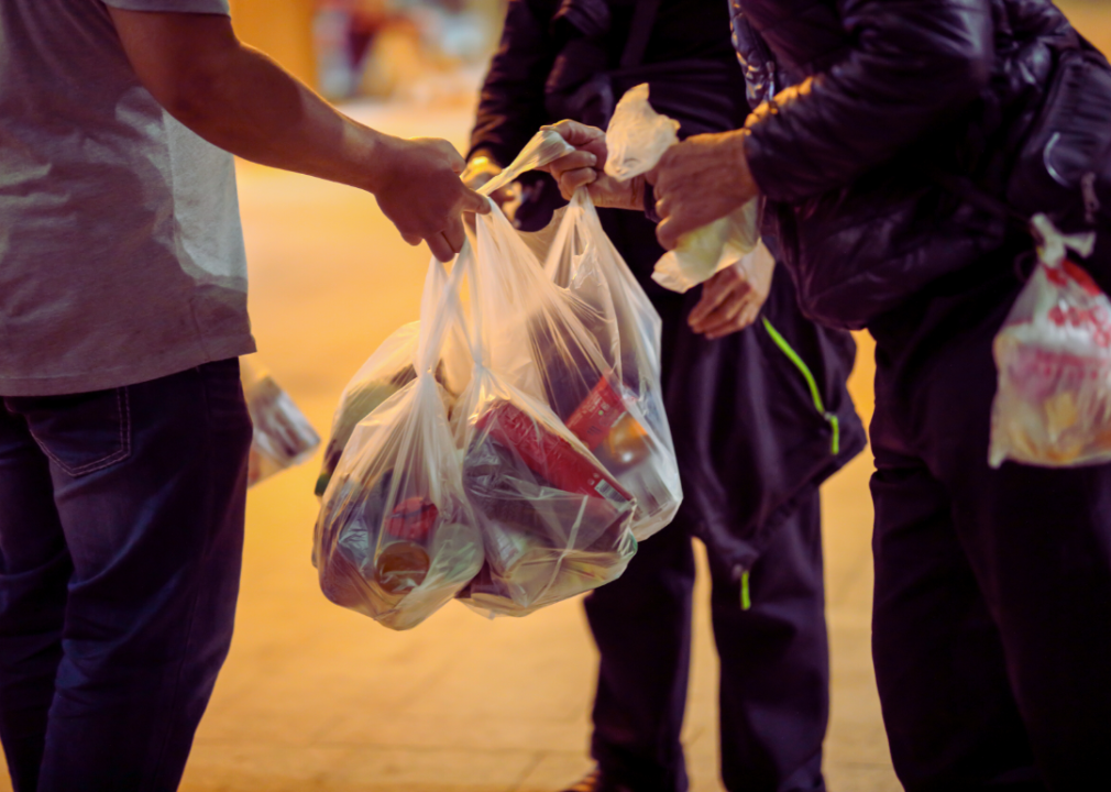 A homeless person accepts bags of food assistance from social workers.
