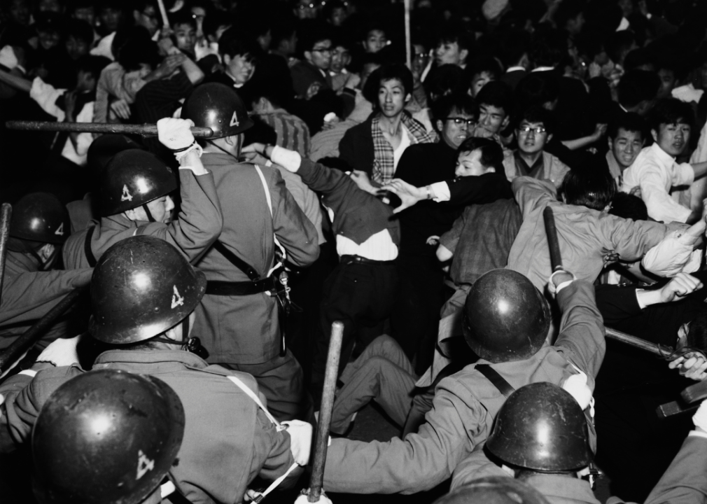 Police with batons fight protestors in a chaotic scene. 