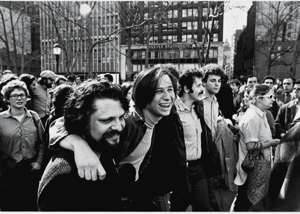 Crowds of protestors in the street, with a focus on a few smiling people with their arms around each other