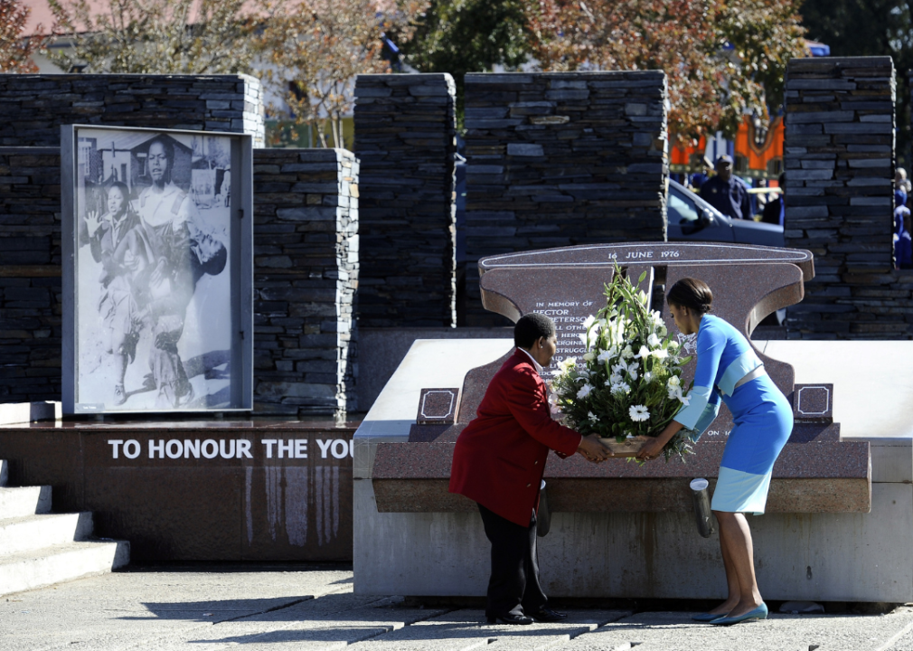 Two people place a large floral arrangement in front of a memorial. 