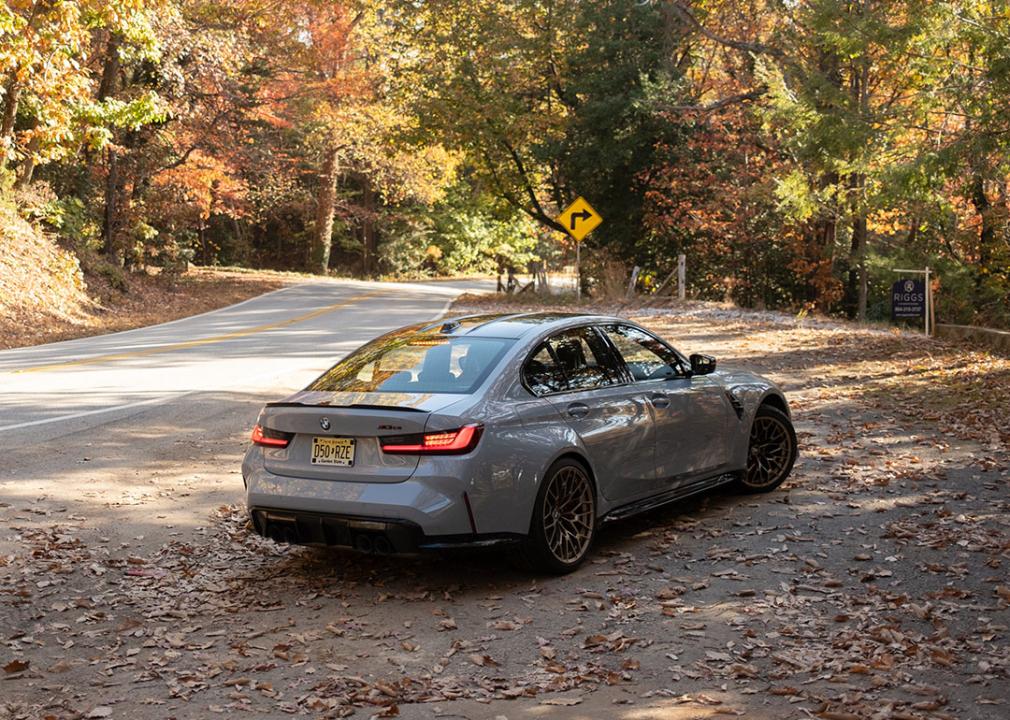 A metallic BMW M3 is parked on a leafy roadside.