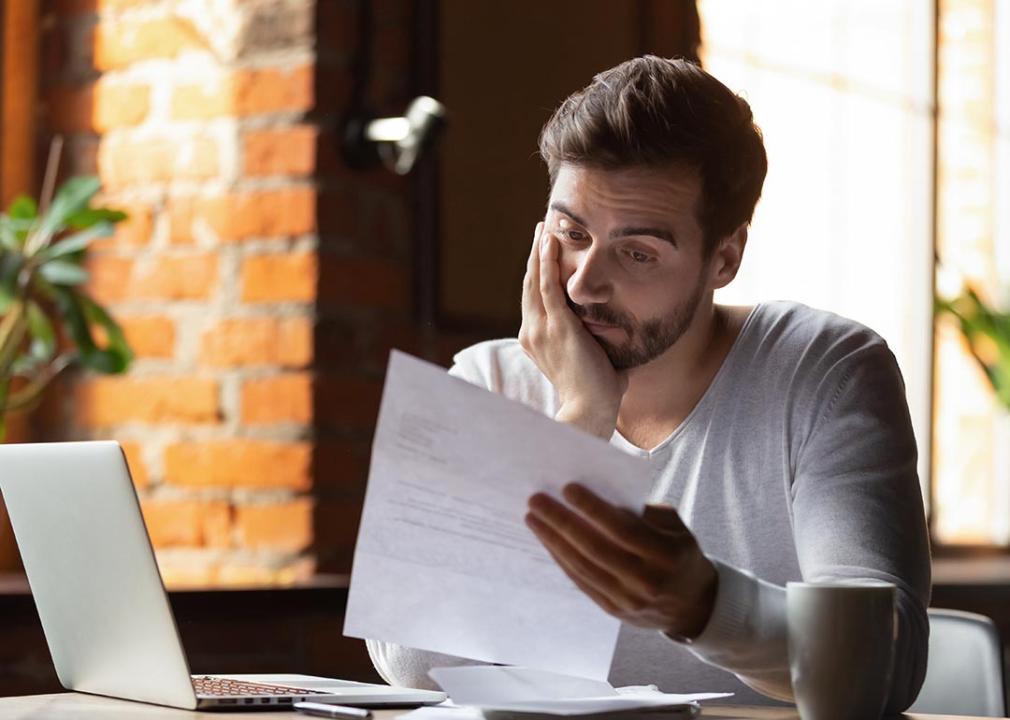 A man working with his laptop while reading a file in deep wonder.