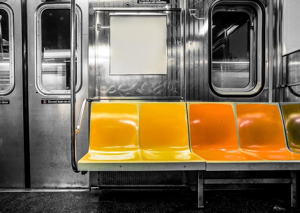 A black and white photograph inside a subway train but the seats are colored in yellow and orange.