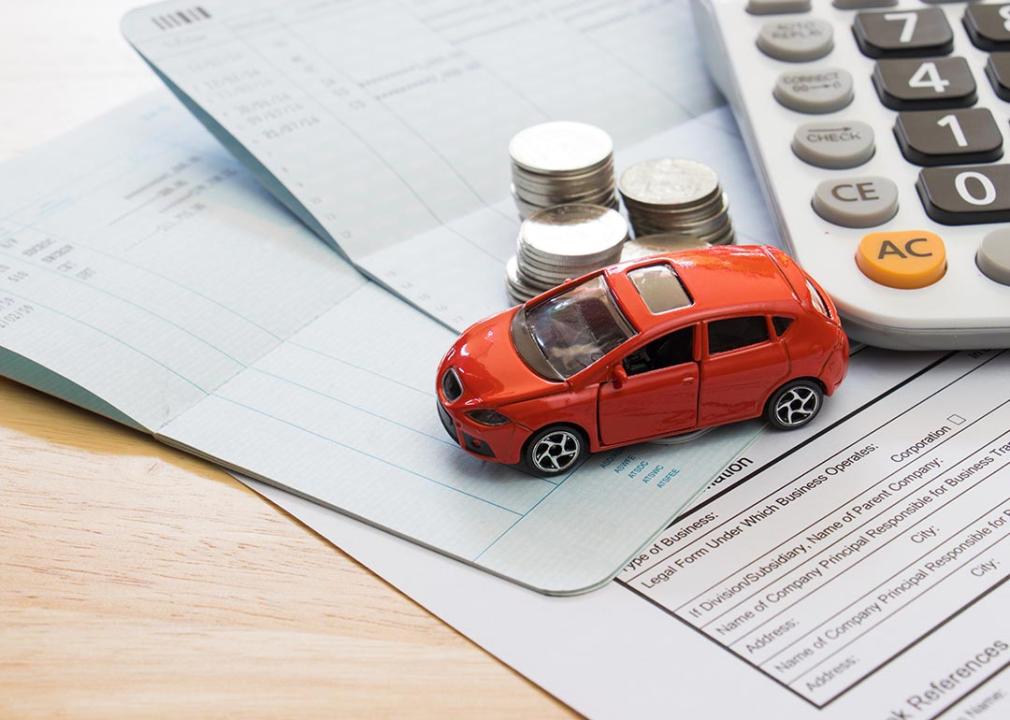 Car insurance bills are seen with a red toy car, coins and a calculator on top of it.