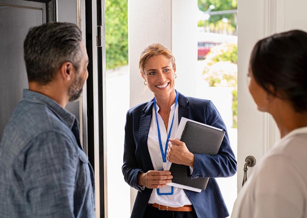 A female entrepreneur happily greeting a couple inside their home.