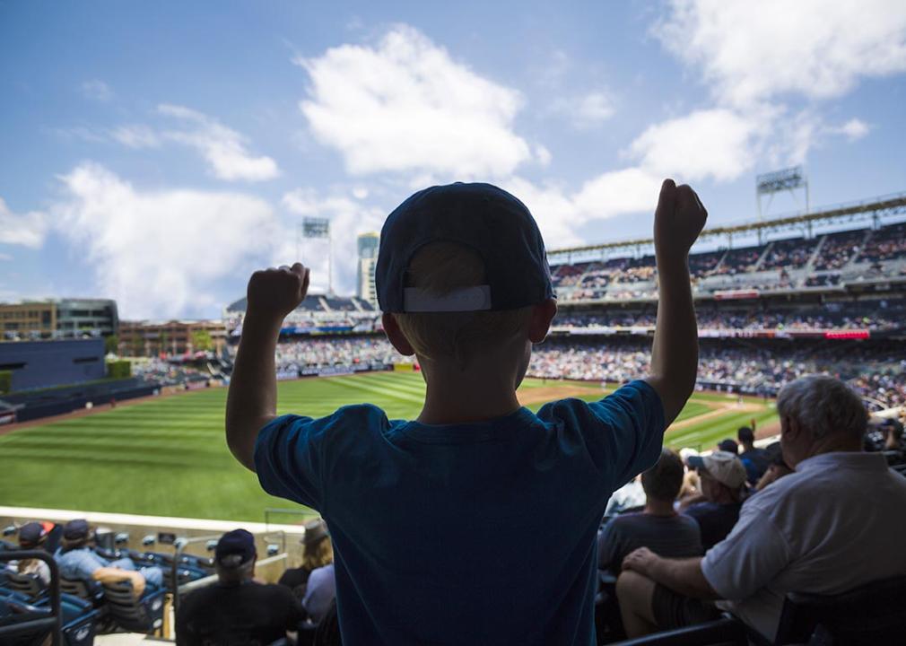 A young boy cheering inside a baseball stadium while facing the field.