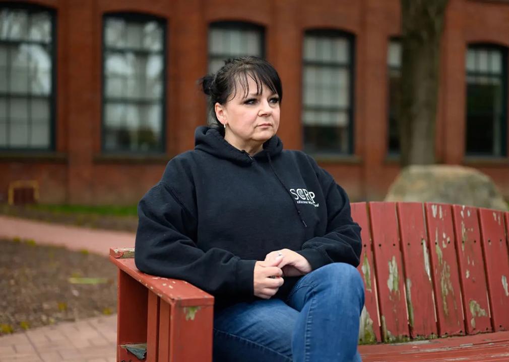 Tracy Shumaker sits on a wooden bench with a back outside her office in Hartford, Connecticut,