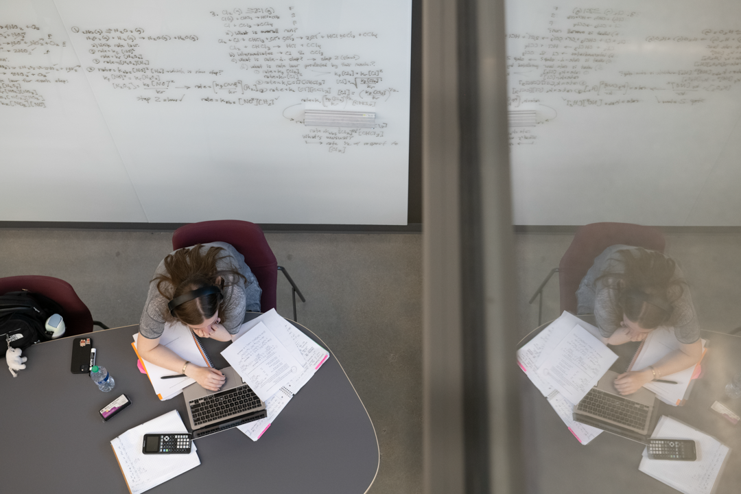 A student at Northeastern University is reflected in a window while studying. 