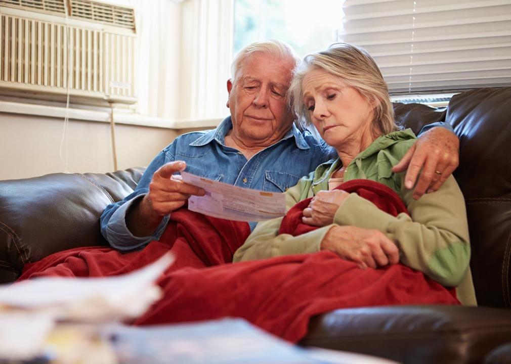 A senior couple sitting together looking worried while reading a bill.