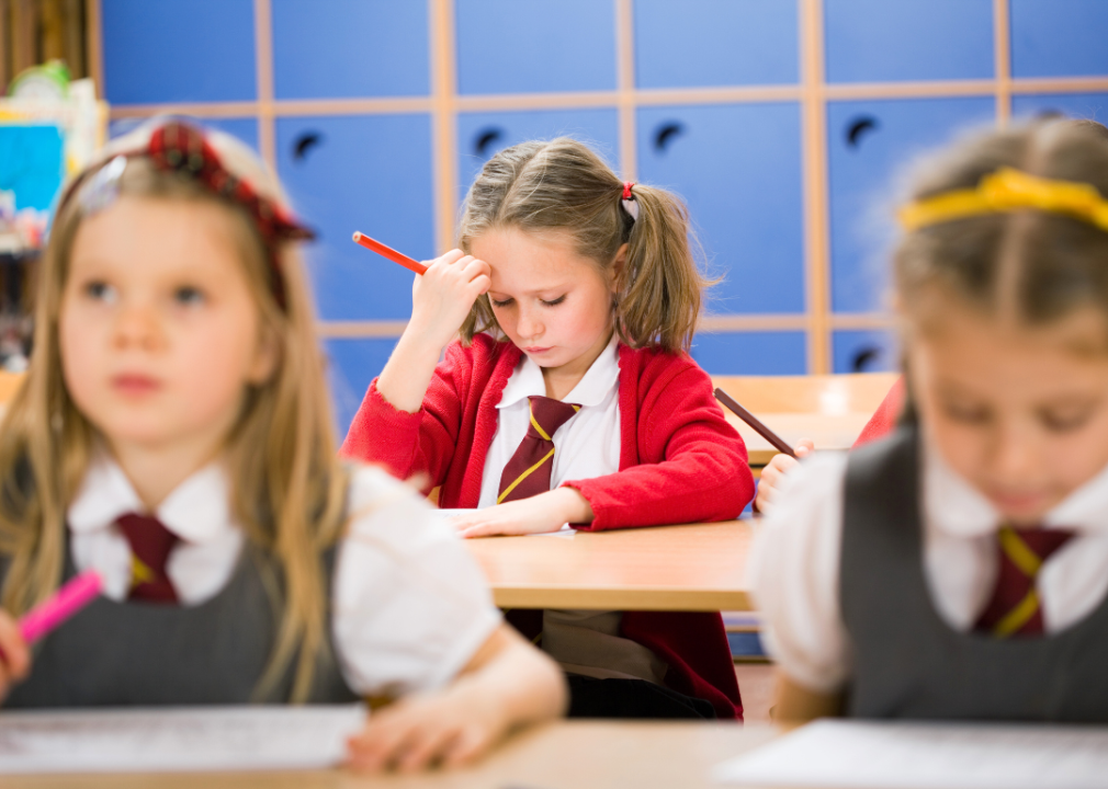 Female child looking down at her desk with frustrated expression as other girls remain attentive in classroom.