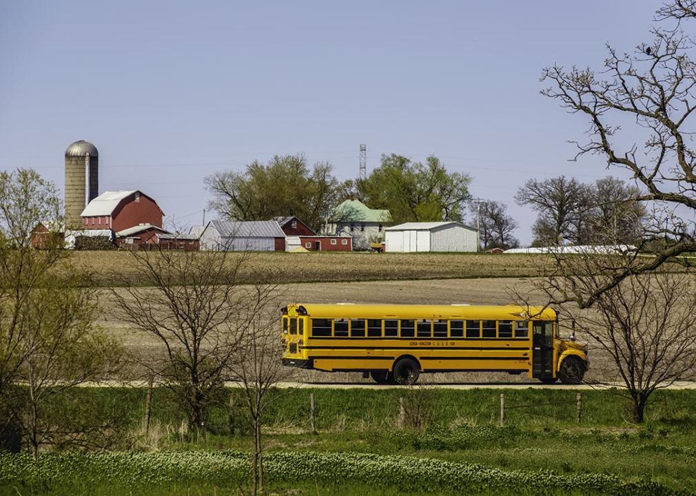 KINGSTON, ILLINOIS A public school bus passes by a large farmstead along a rural road on a spring day, with the edge of a county forest preserve in the foreground.