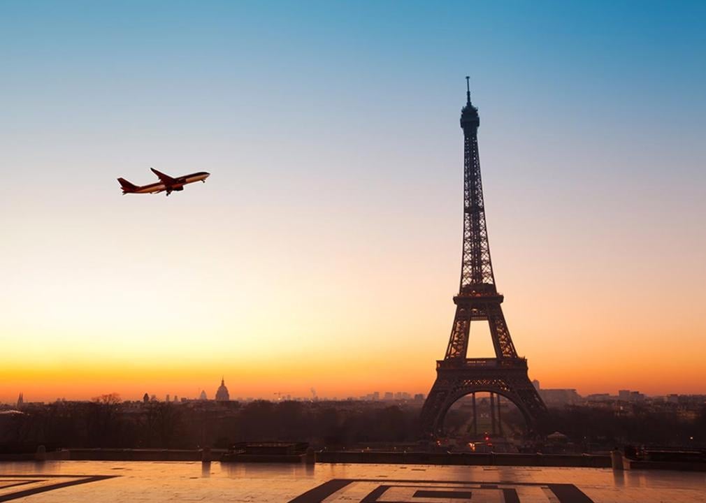 View of the Eiffel Tower during sunset with a plane seen flying over.