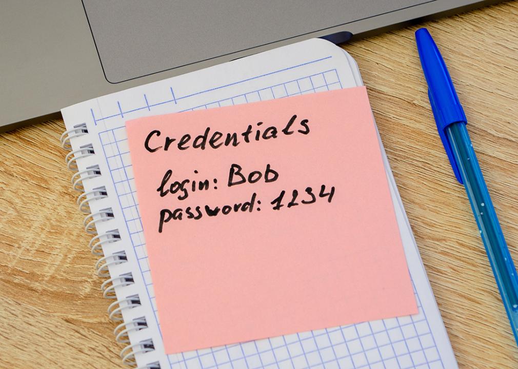 Simple user and password credentials written on a sticky note that lies on a notebook next to a laptop. 