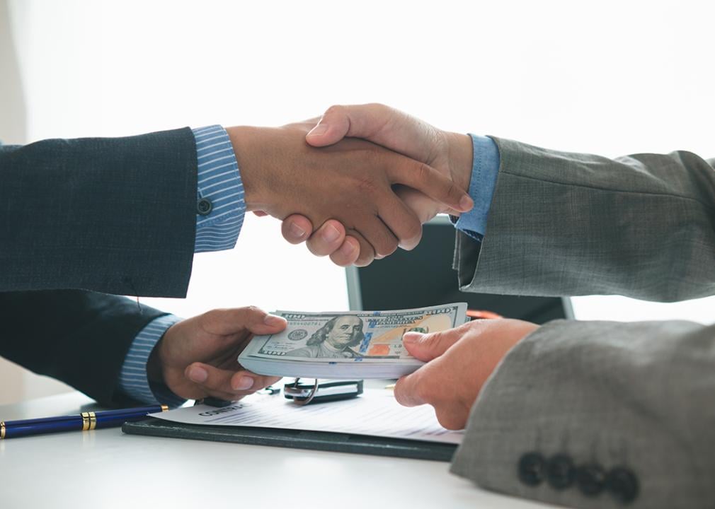 A client and car dealer shake hands after agreeing to a sales contract.