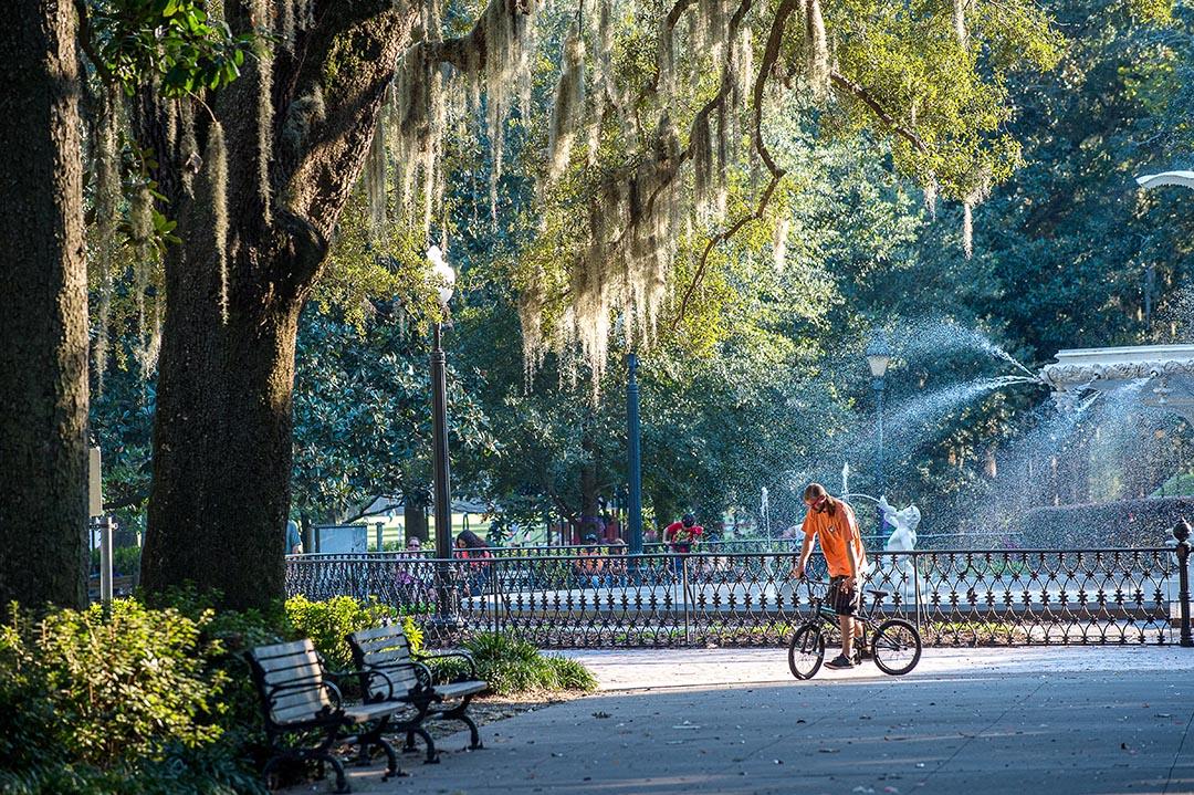 Forsyth Park fountain in Savannah, GA in October with a man in an orange shirt walking his BMX bike. 