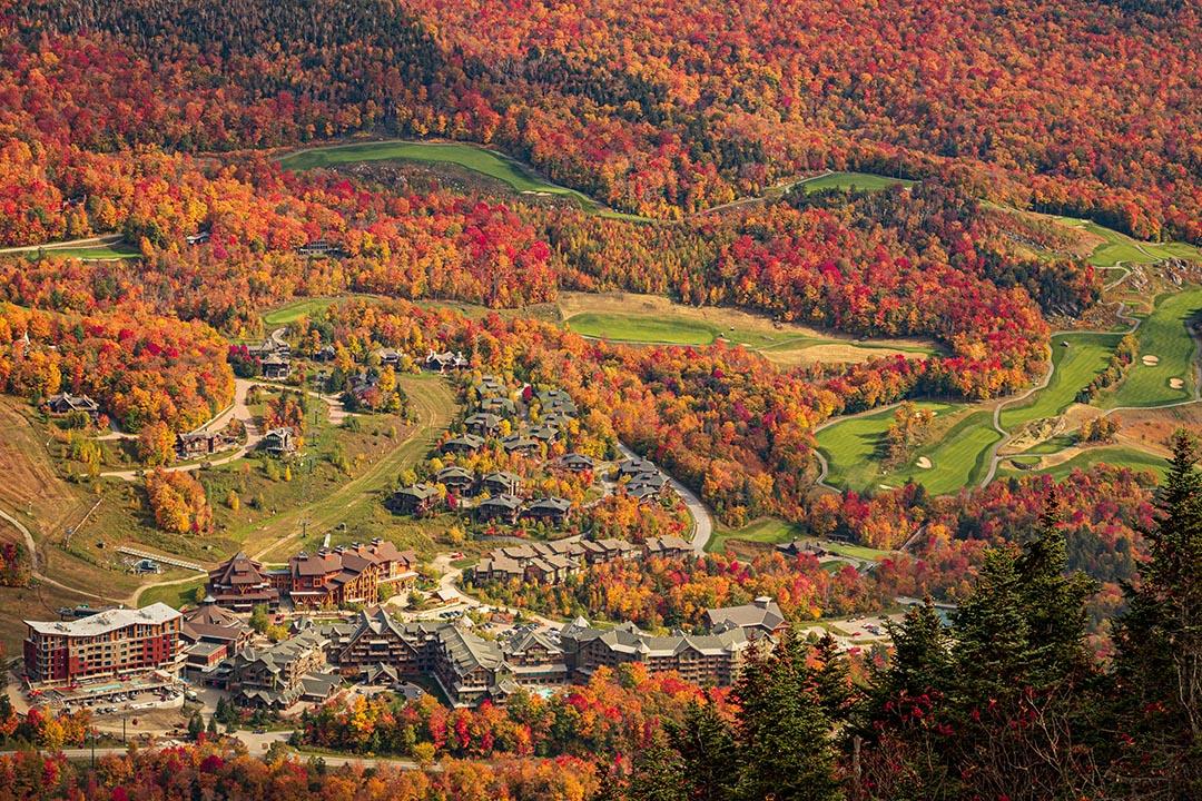 Stowe Mountain Resort in Stowe Vermont with autumn foliage around a green golf course.