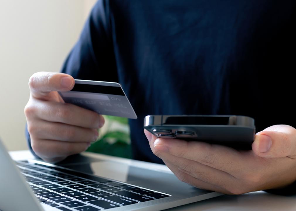 A person holding a credit card, making a purchase payment using a laptop and a phone.