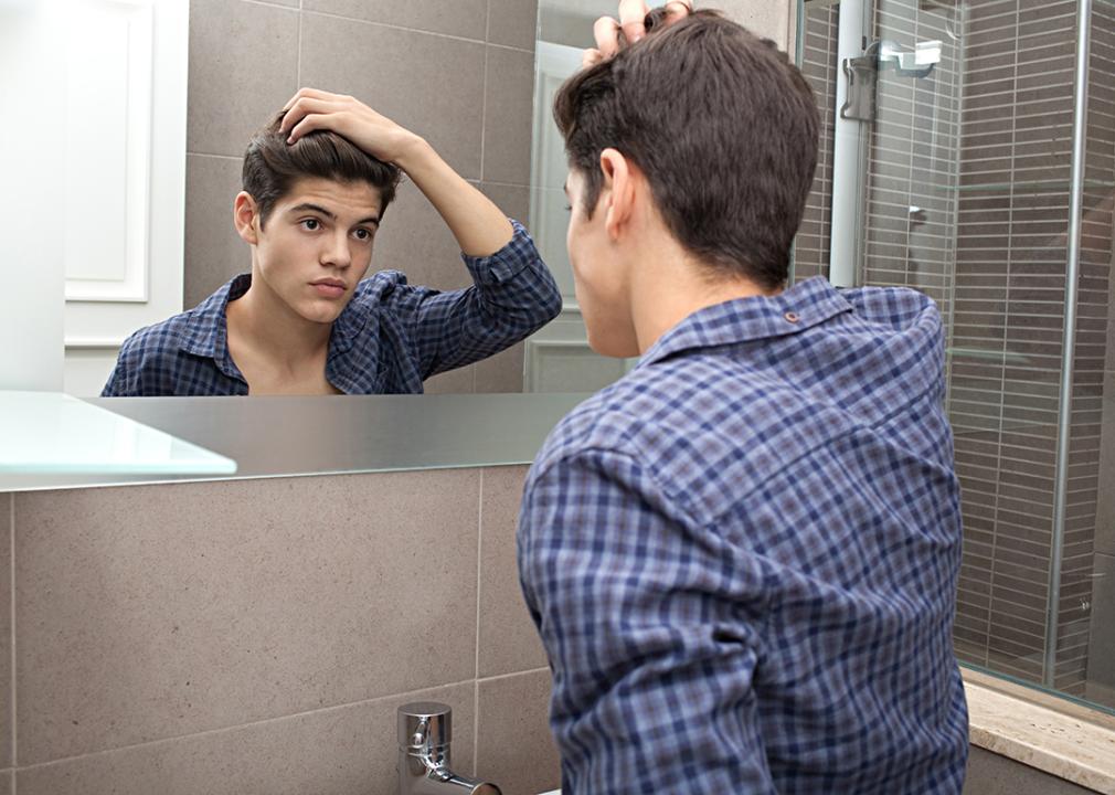 Young teenage man looking at himself in a bathroom mirror at home doing his hair.