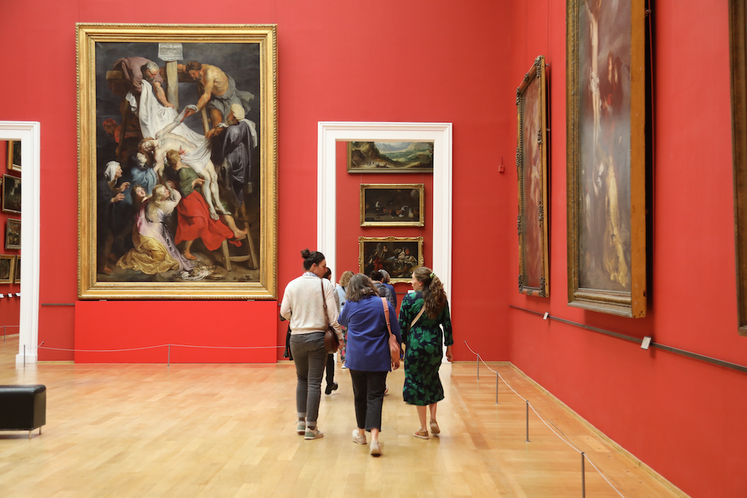 Museum visitors walk through an exhibition with art on red-orange walls inside Lille’s Palais des Beaux-Arts. 