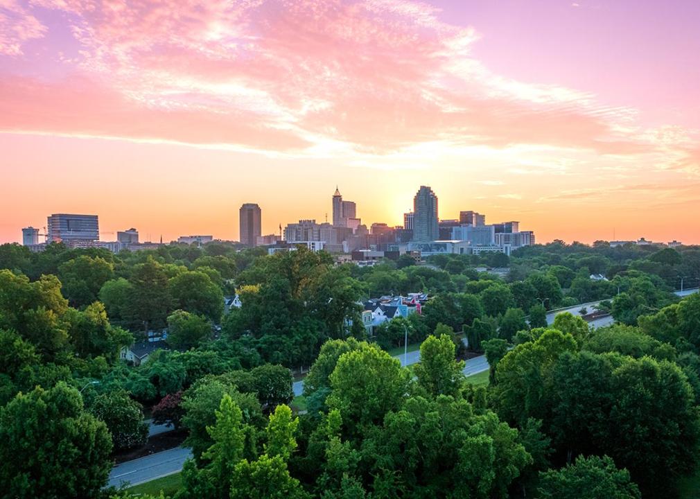 A view of Raleigh, N.C. skyline at sunrise with large trees in the foreground. 