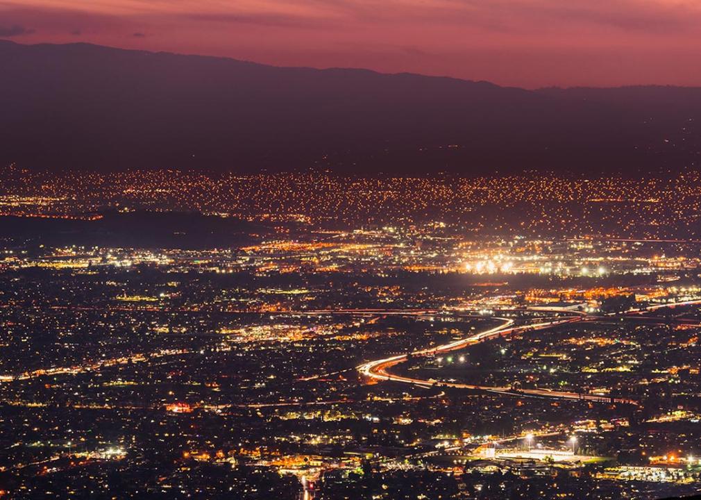 Panoramic night view of urban sprawl in San Jose, Silicon Valley, California; Visible light trail left by cars driving on one of the freeways.