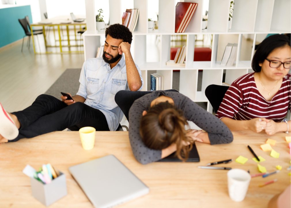 Three distracted young coworkers at a table.