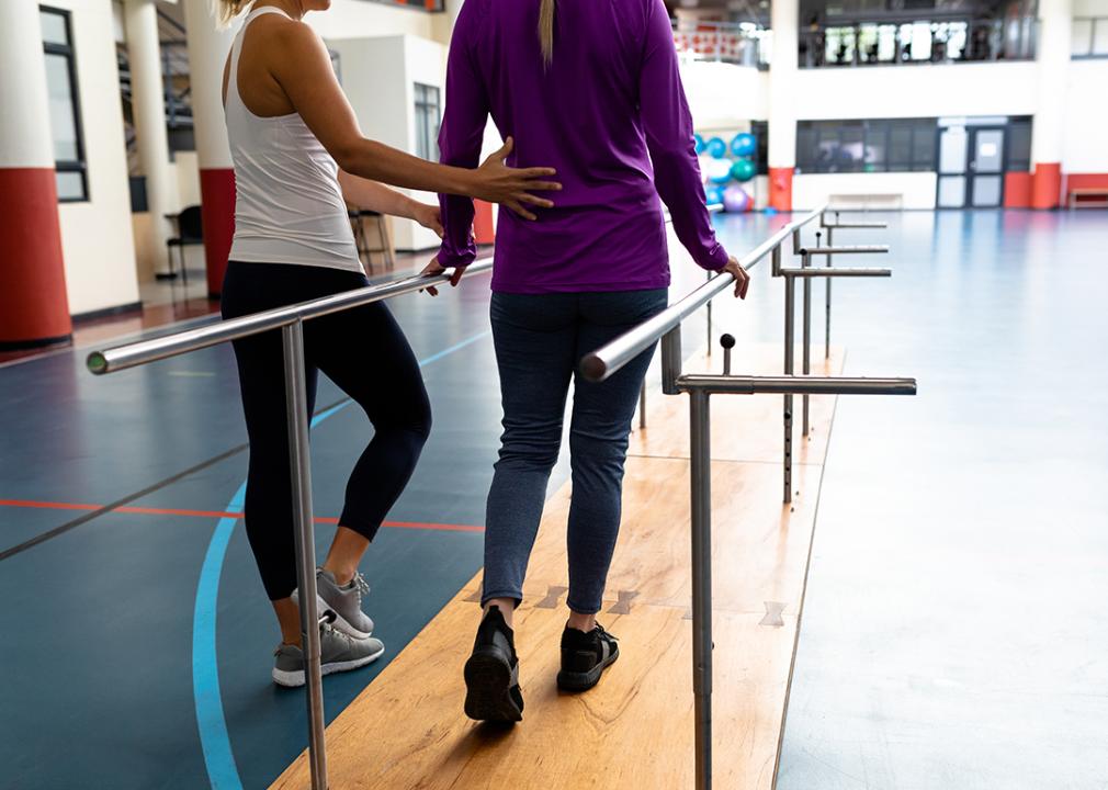 A female physical therapists assist a patient in a walking practice.