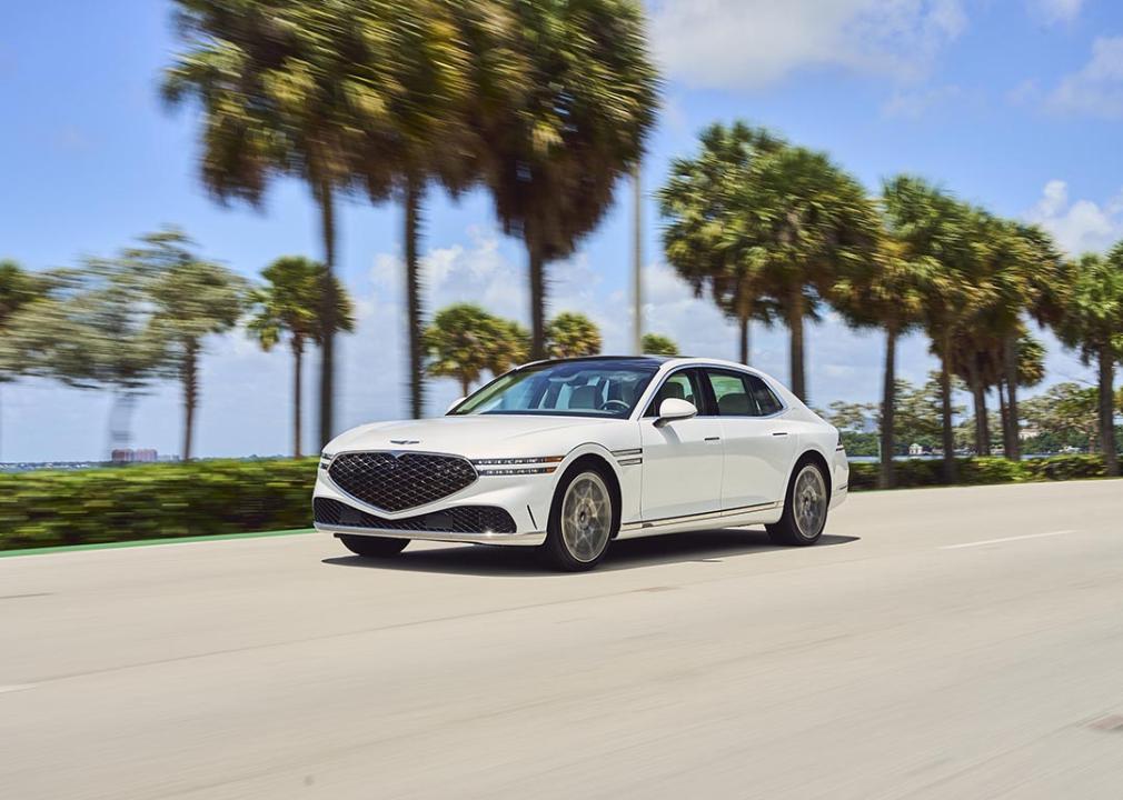 White Genesis G90 on the road with palm trees and sky in the background.