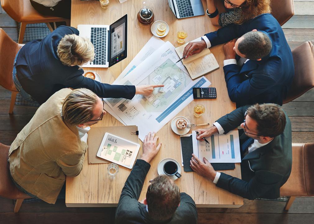 Professionals from an architect business are gathered in a table meeting with food and business documents at the center.