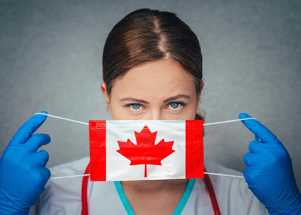 A female nurse putting on a mask printed with a Canadian flag.