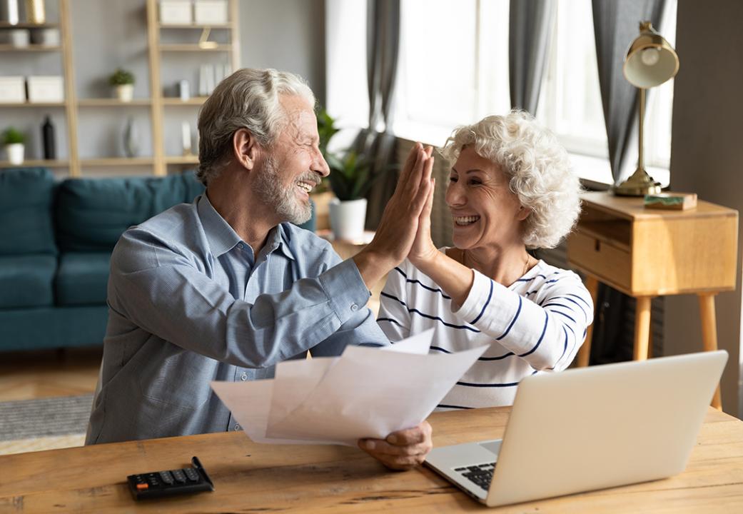 A baby boomer couple giving each other high five while doing finances.