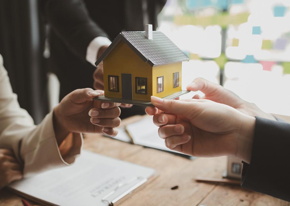 A conceptual image showing three people holding a house figure to represent investing in a real estate.