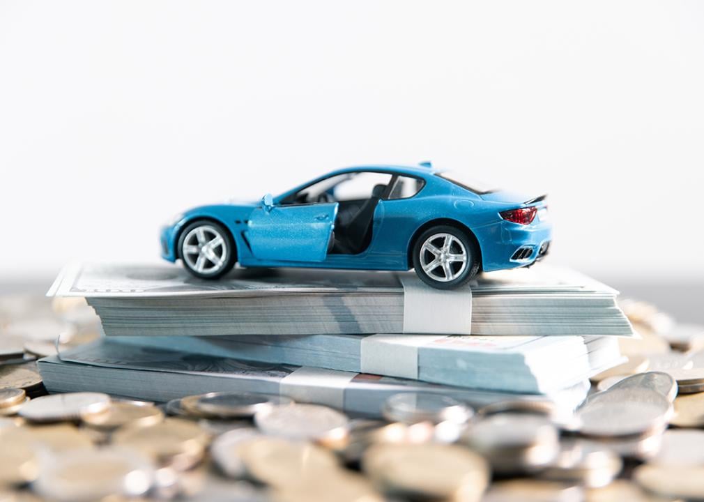 A blue car on top of a stack of money and coins.